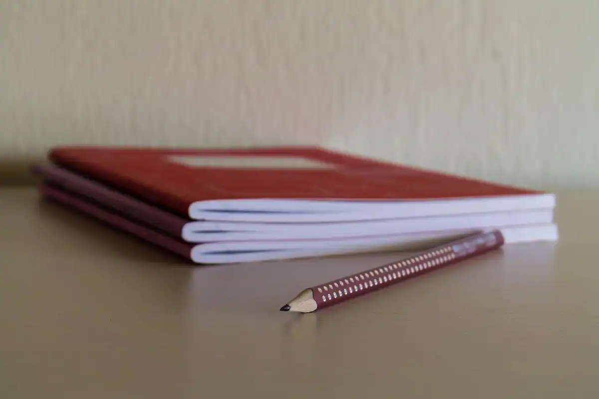 Caiet deschis și creion pe un birou maro, lângă un laptop, pentru un curs plătit de firmă