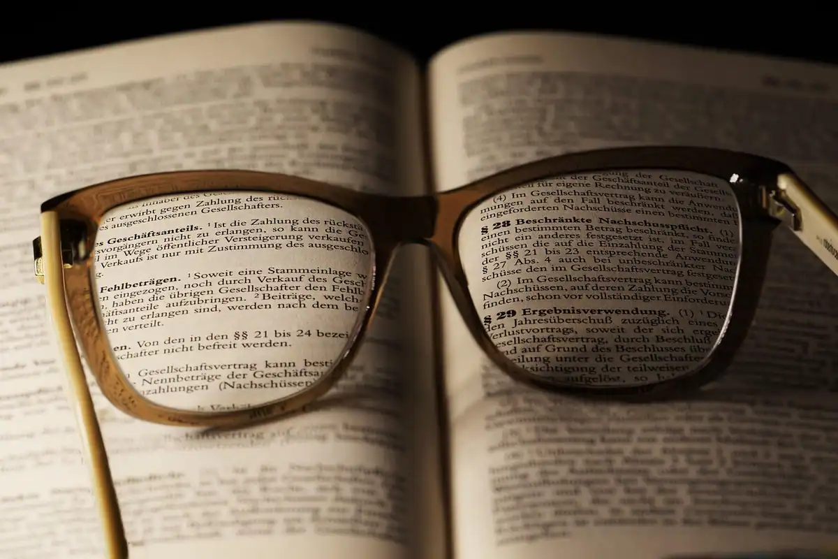 Pagină de text văzută printre lentilele unor ochelari, ca la verificarea unui contract