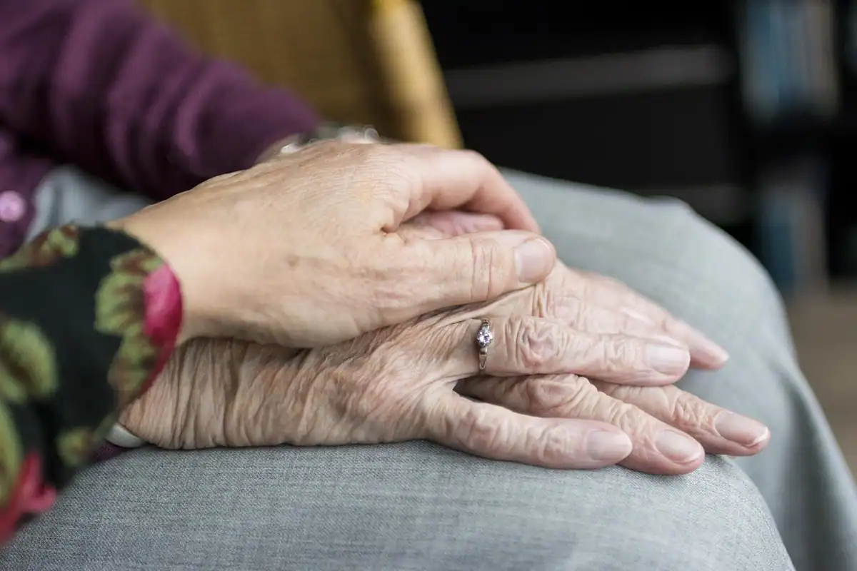 Mâini ale unei persoane în vârstă, ținute cu grijă de cineva care o îngrijește