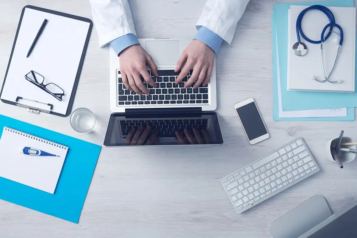 Birou cu laptop, stetoscop și clipboard, la verificarea unui certificat medical