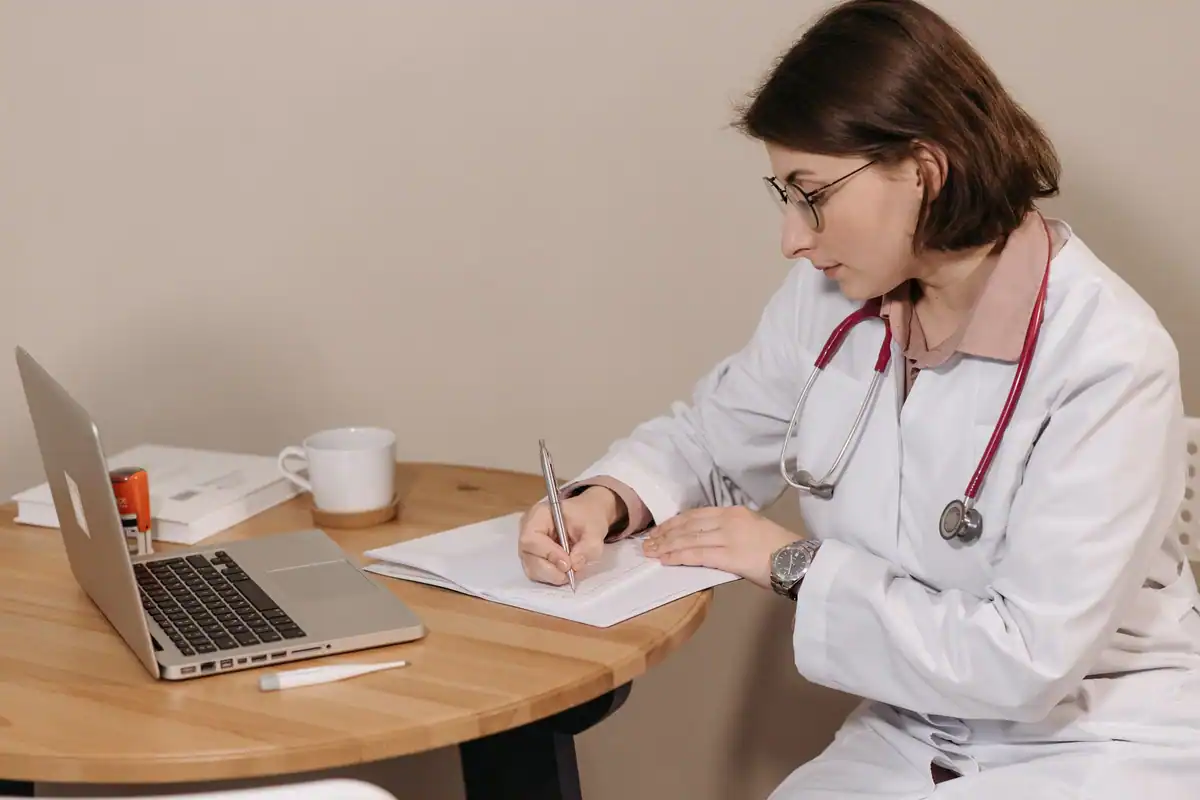 Medic care completează un certificat la birou, lângă un laptop