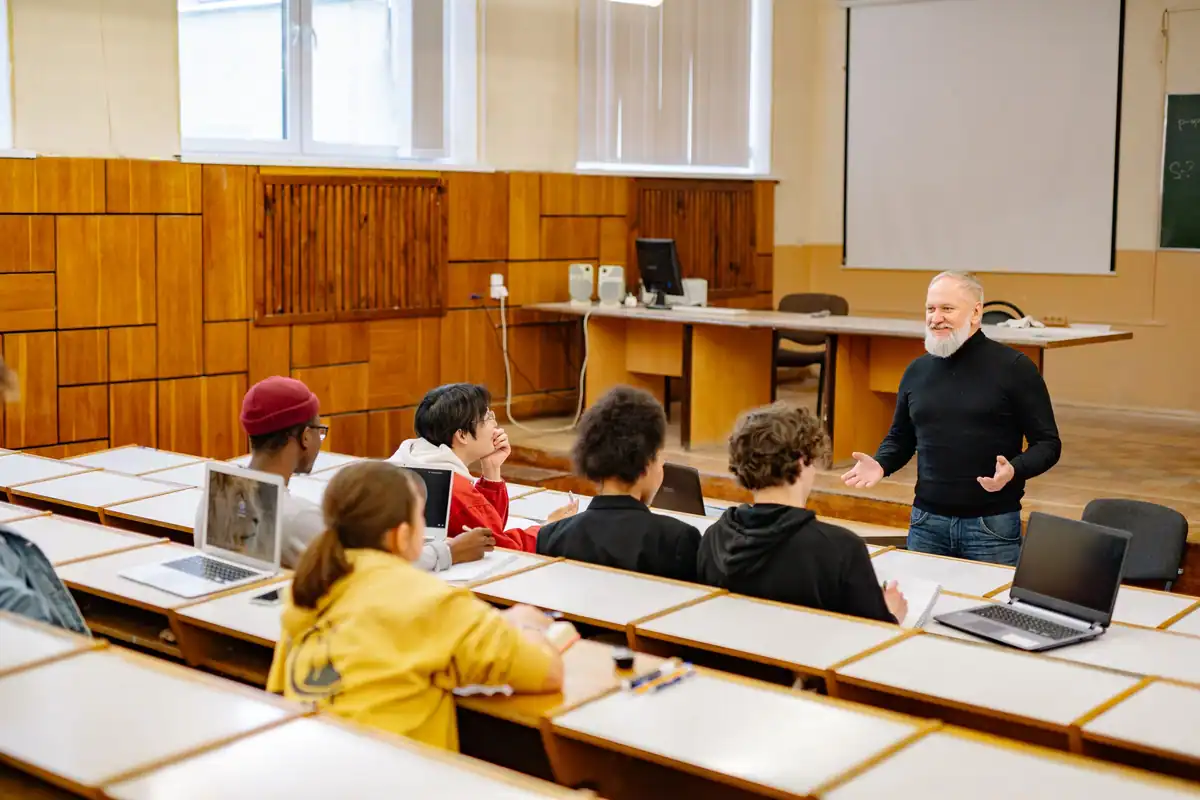 Cursanți și lector într-o sală de curs, cu laptopuri pe bănci