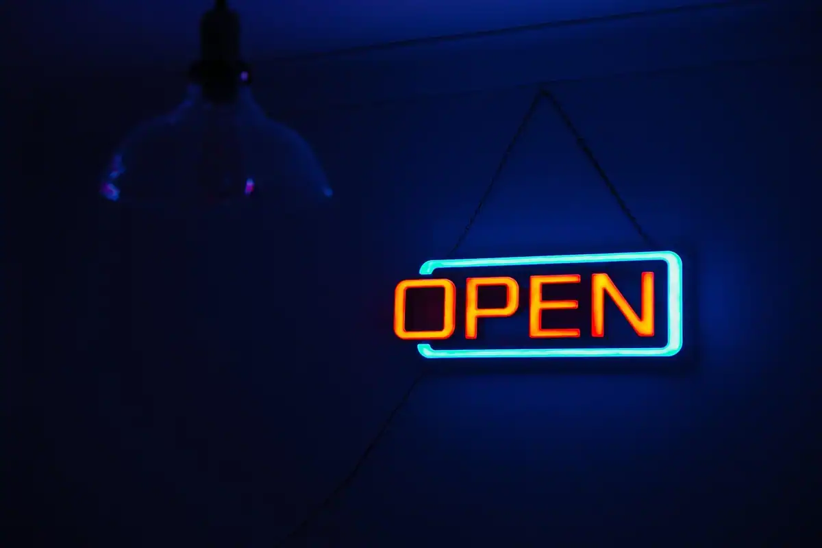 Firmă luminoasă cu neon Open aprinsă pe un perete întunecat, pentru programul de lucru