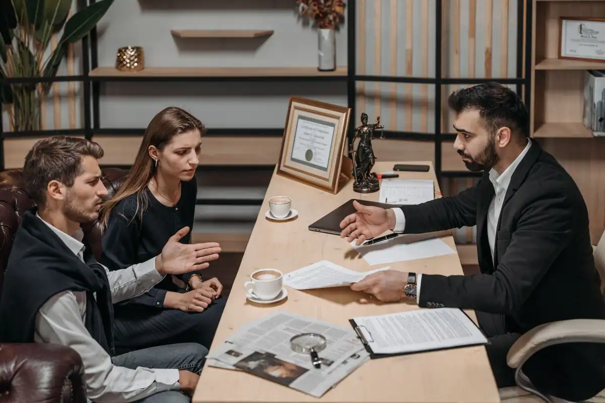 Avocat care discută cu doi clienți, cu documente pe masa de consultanță
