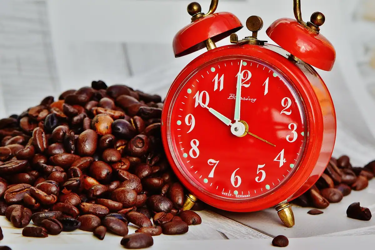 Ceas deșteptător roșu printre boabe de cafea, pentru programul redus de lucru