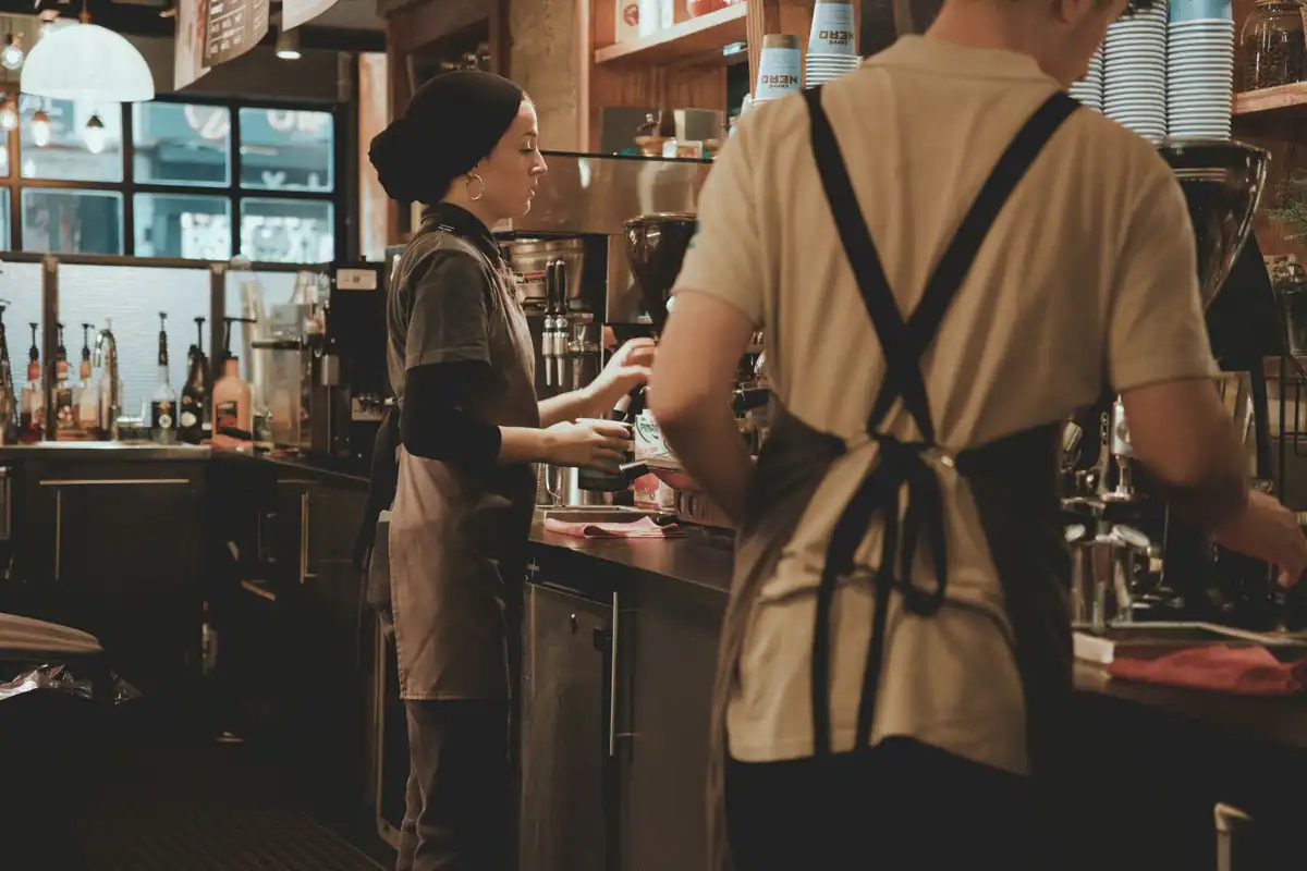 Baristi la lucru într-o cafenea, pregătind băuturi în timpul programului redus