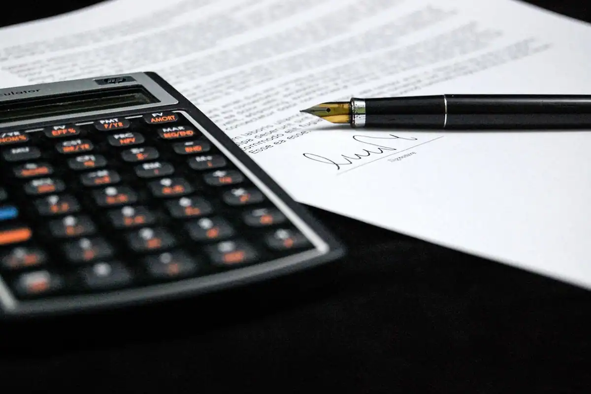 Contract semnat cu stiloul, lângă un calculator de birou, la încheierea angajării
