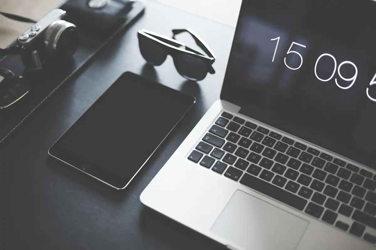 Spațiu de lucru cu laptop Apple, tabletă, ochelari de soare și cameră foto, lângă un ecran