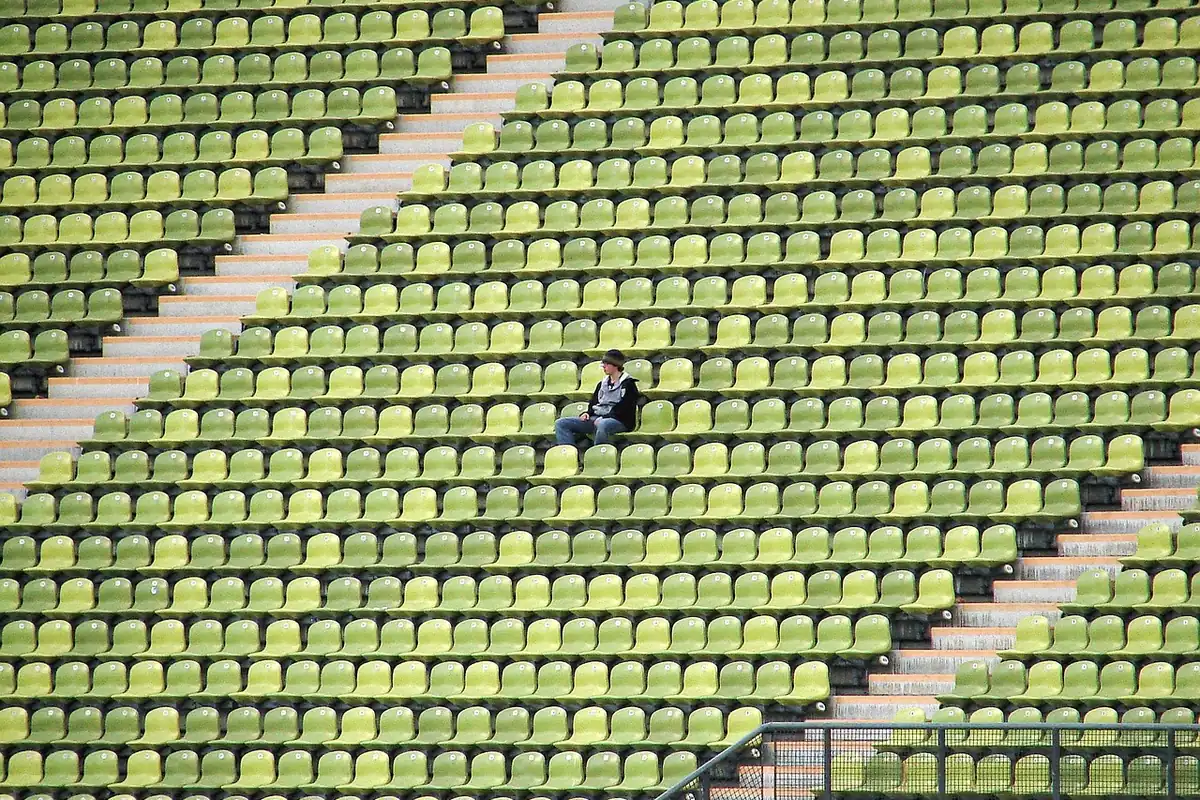 Om singur așezat pe un rând de scaune goale într-un stadion mare, cu multe locuri libere