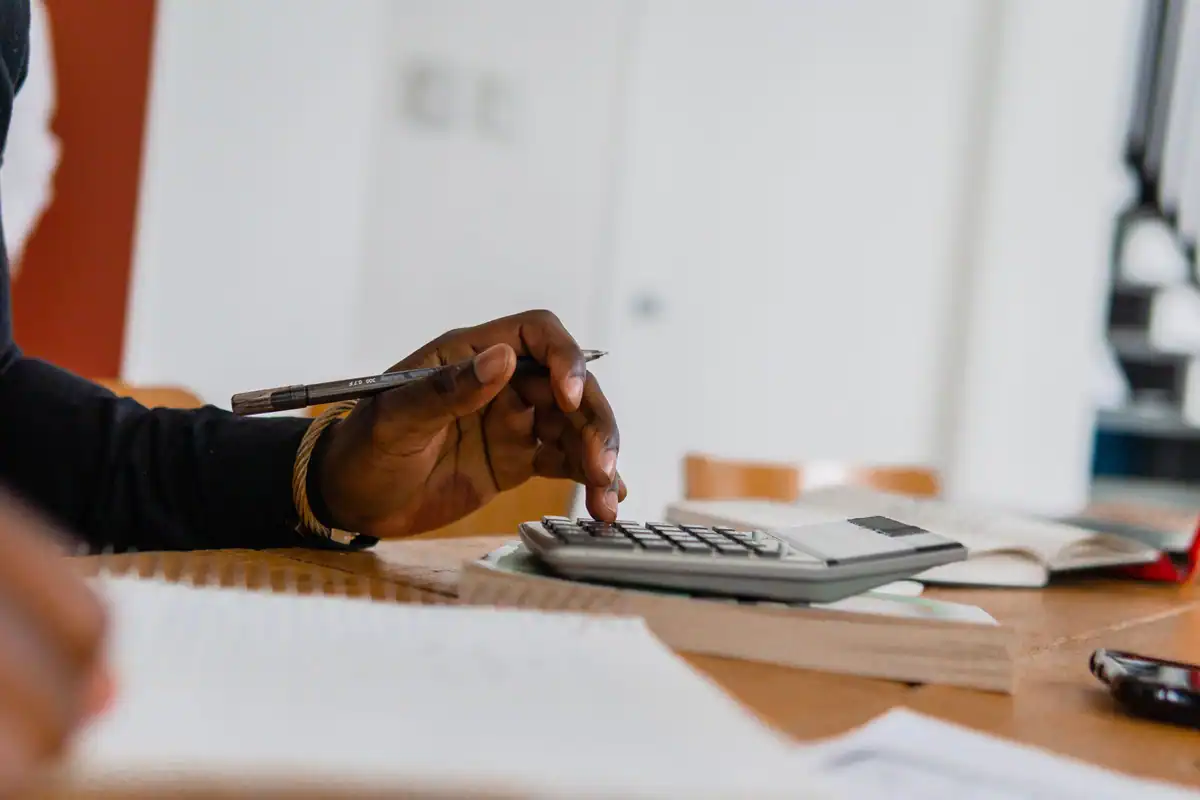 Persoană care folosește calculatorul și pixul pentru verificarea sumelor din fluturaș