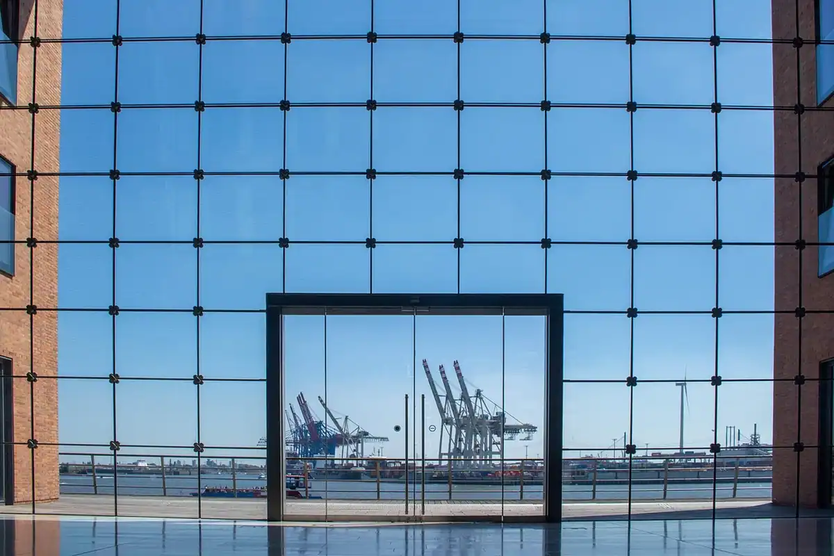Clădire cu ferestre mari de sticlă lângă apă, într-un port cu o macara în fundal