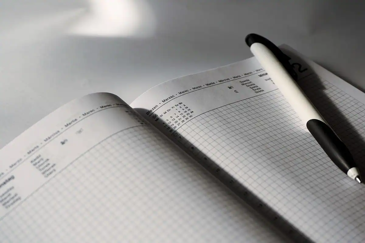 Pagină de calendar cu o dată încercuită cu pixul și o agendă deschisă pe un birou