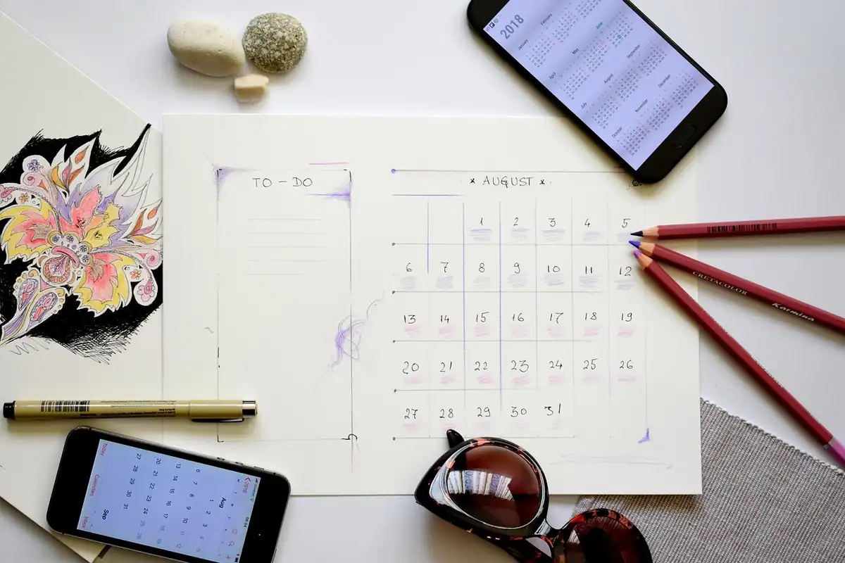 Planner deschis cu calendarul lunii august și zilele de vacanță notate, pe o masă
