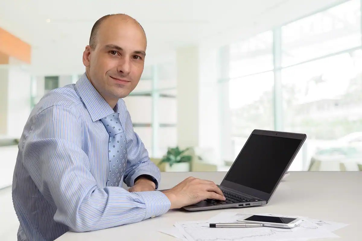 Bărbat zâmbitor la laptop într-un birou, un angajat profesionist la locul lui de muncă