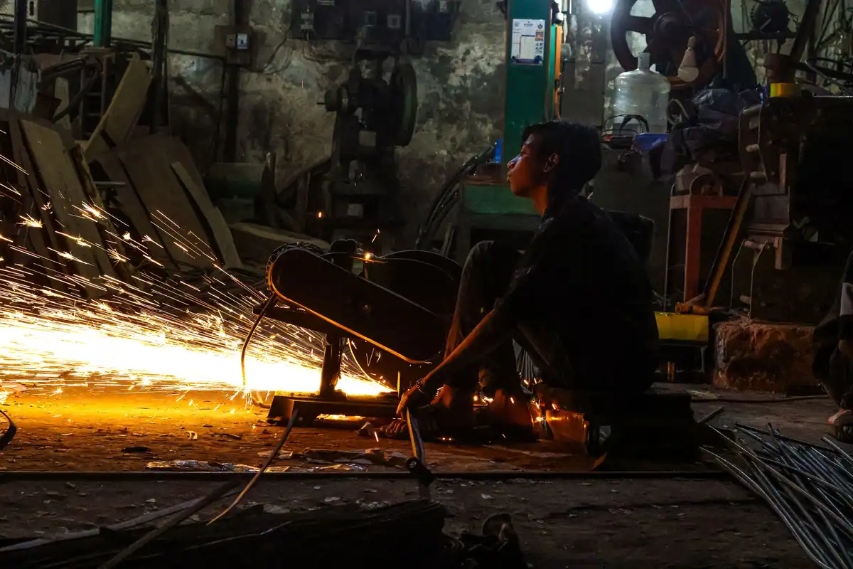 Muncitor în atelier slab luminat, cu scântei care țâșnesc de la un utilaj