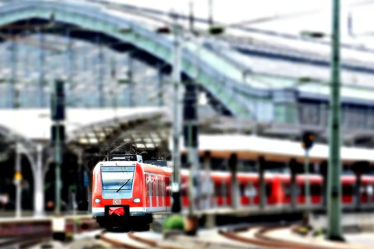 Peron de gară cu șine și un tren sosind, la o stație centrală dintr-un oraș mare