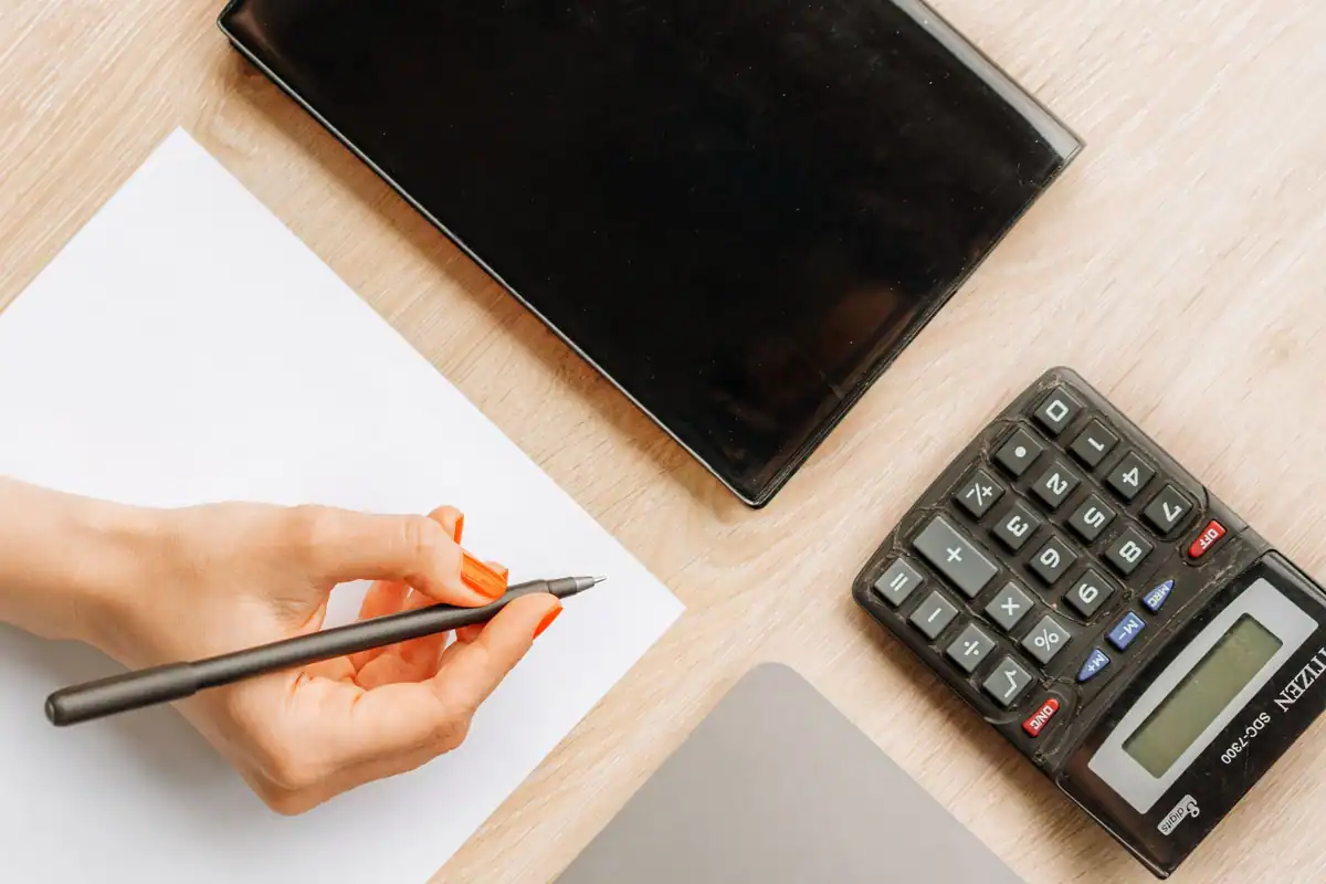Mână care scrie lângă un calculator, în calculul sumelor reținute din salariu