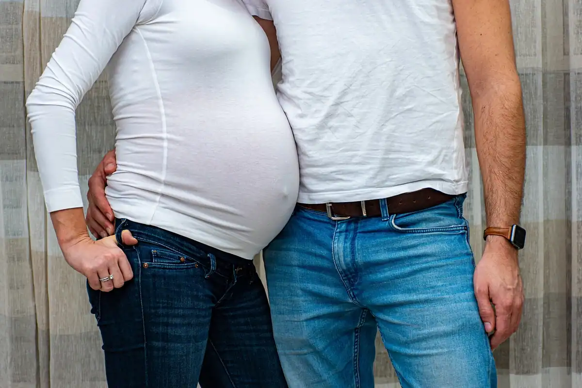 Cuplu de părinți în așteptarea unui copil, cu burta de gravidă în prim-plan, într-un portret de familie