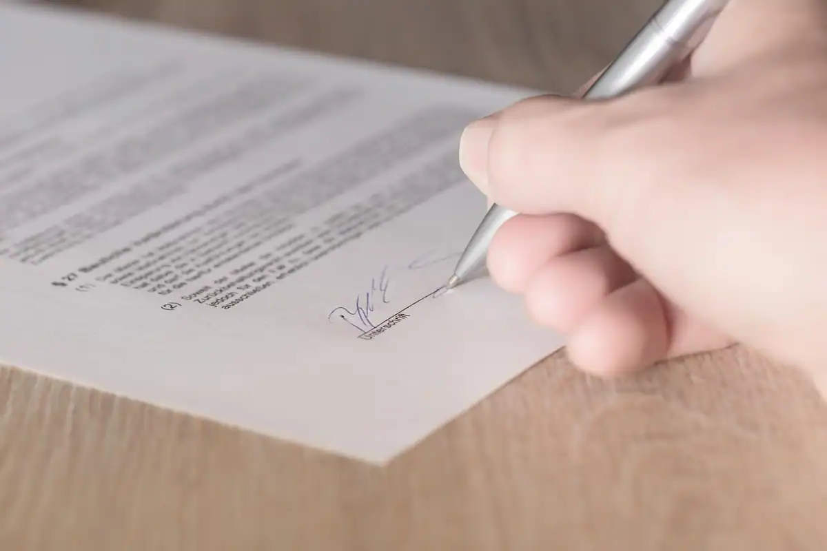 Mână care semnează un contract pe hârtie, la încheierea unei înțelegeri colective
