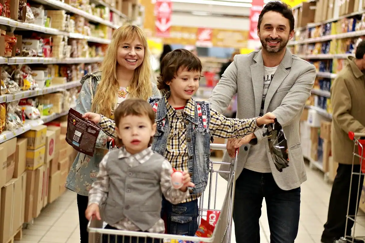 Familie veselă cu copii, care face cumpărături cu un cărucior într-un magazin alimentar